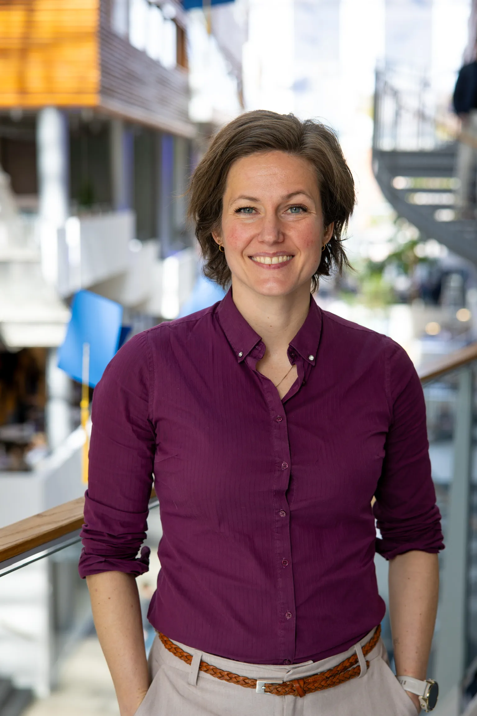 Portrett av Maya Krogstad, smilende i en lys atriumbygning.