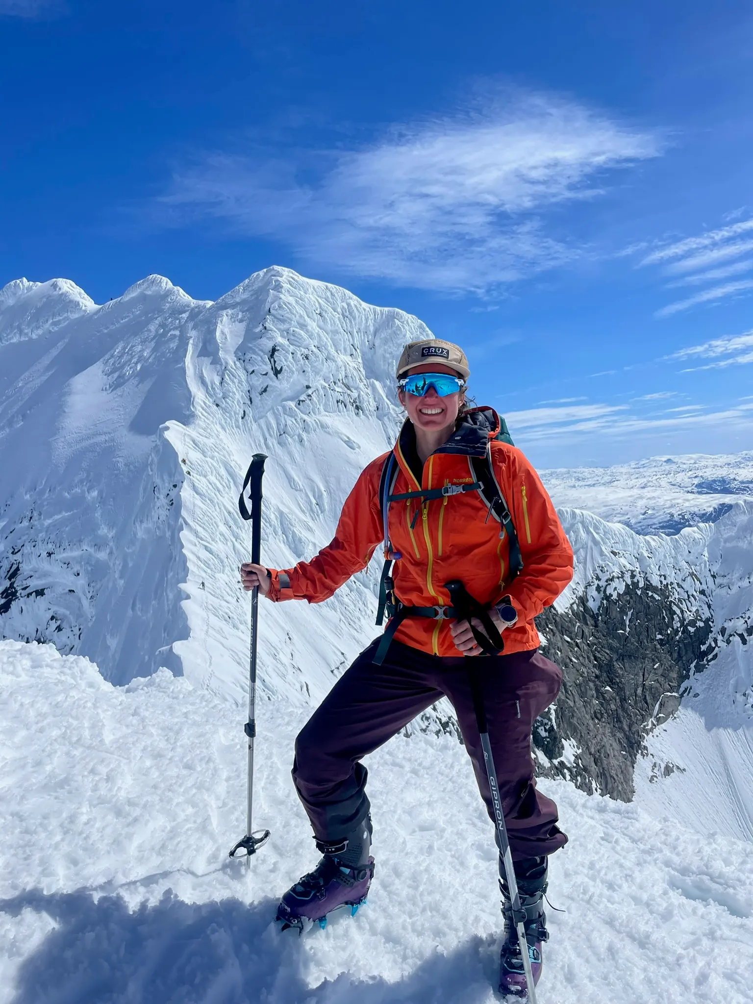 Maya på topptur, smilende foran en snødekt fjellrygg.