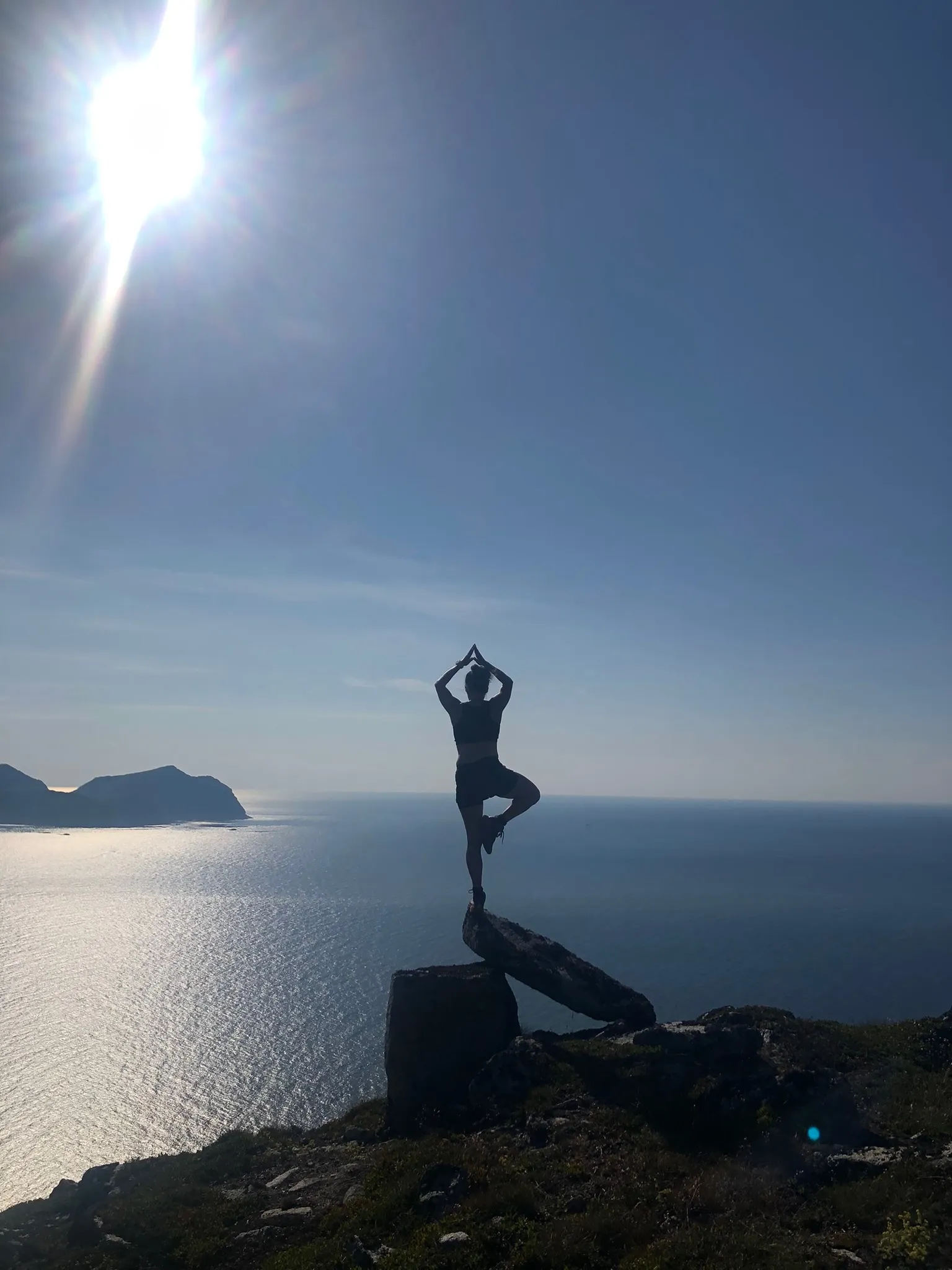 Maya står i yogaposisjon på en steinblokk høyt over havet.